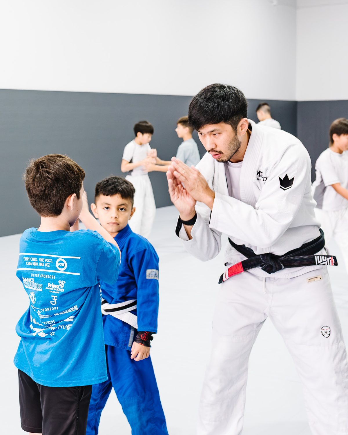 Coach Brian Yi, Brazilian Jiu-Jitsu black belt, demonstrating a technique for two young students at MOMO BJJ in Frisco