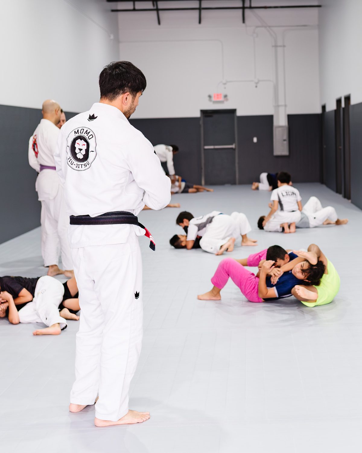 Coach Brian Yi supervising kids practicing Jiu-Jitsu with partners during a MOMO BJJ kids class