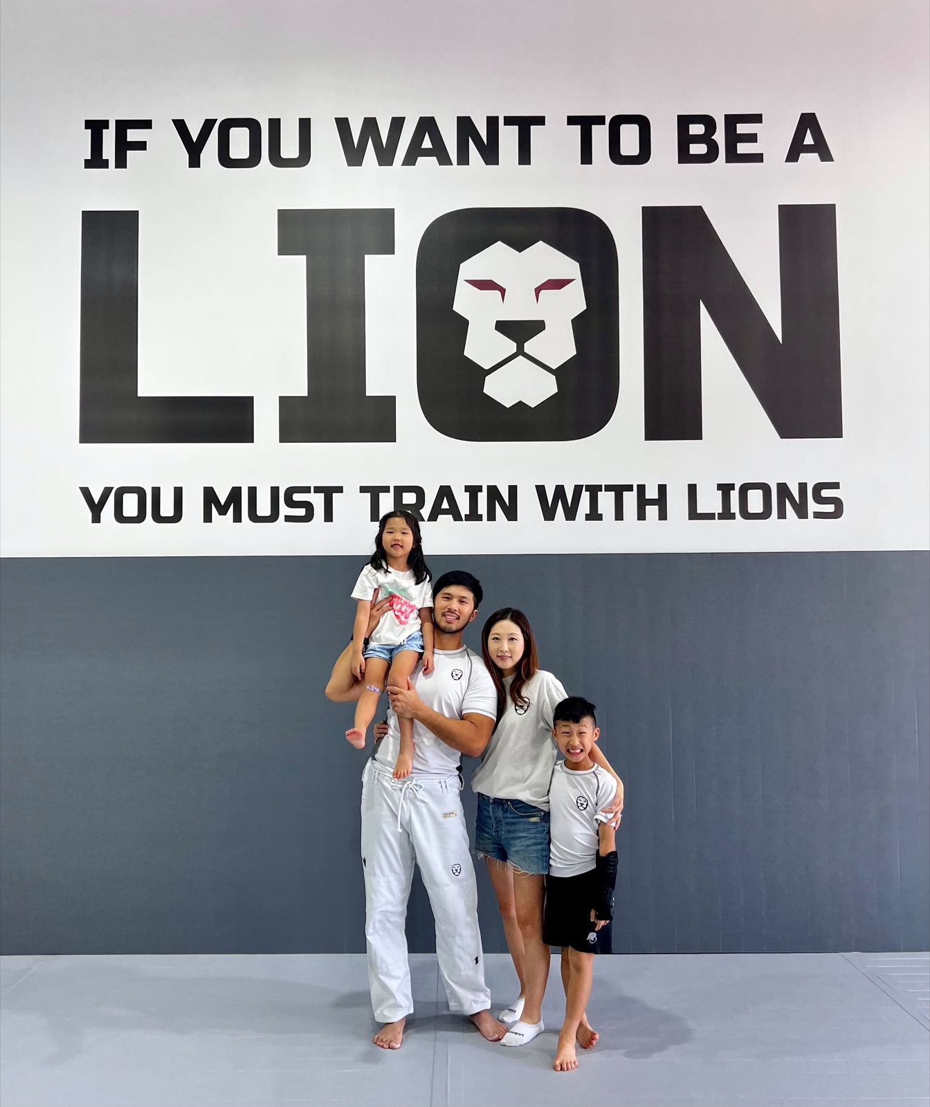 Brian Yi with his wife and two children under the MOMO BJJ LION mural