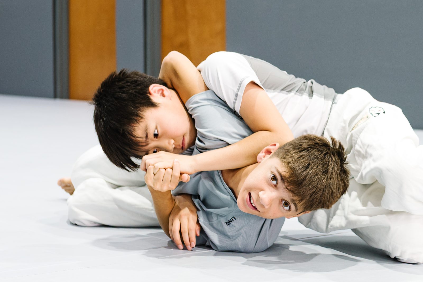 Two kids practicing Jiu-Jitsu together at MOMO BJJ, one smiling at the camera